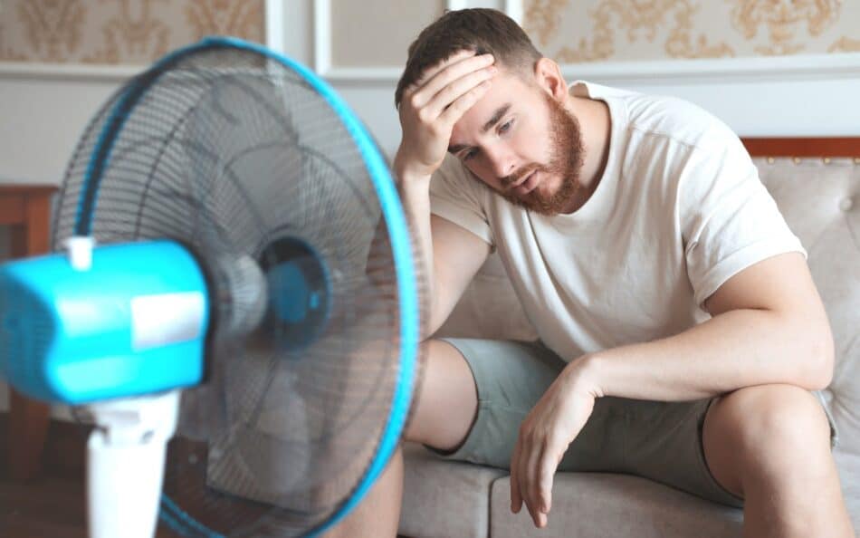 Man sitting in front of fan looking overheated.